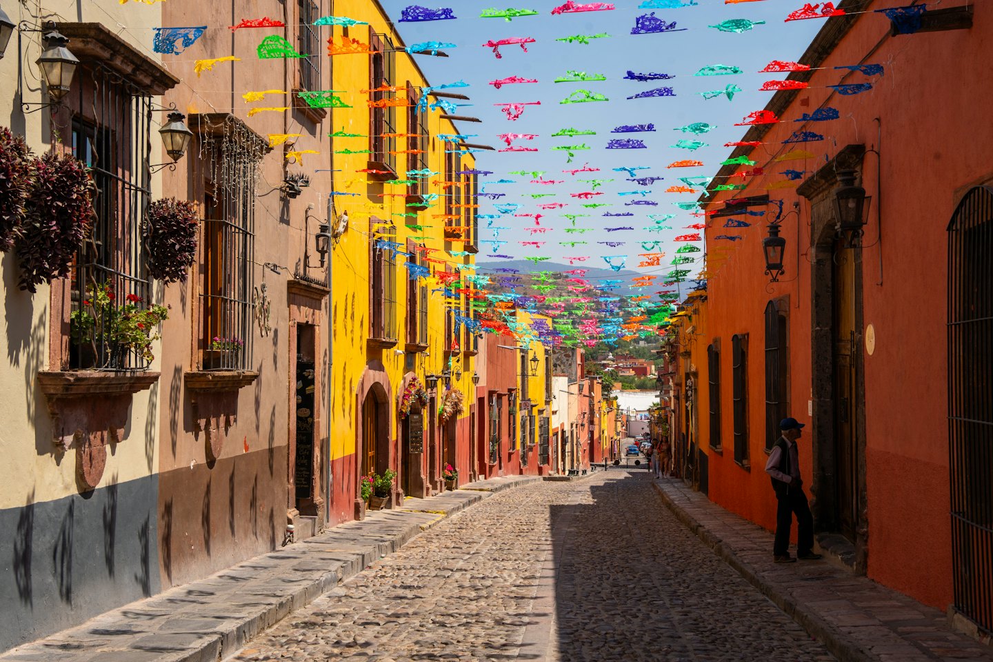 Hombre de pie en una calle adoquinada decorada con pancartas colgantes.